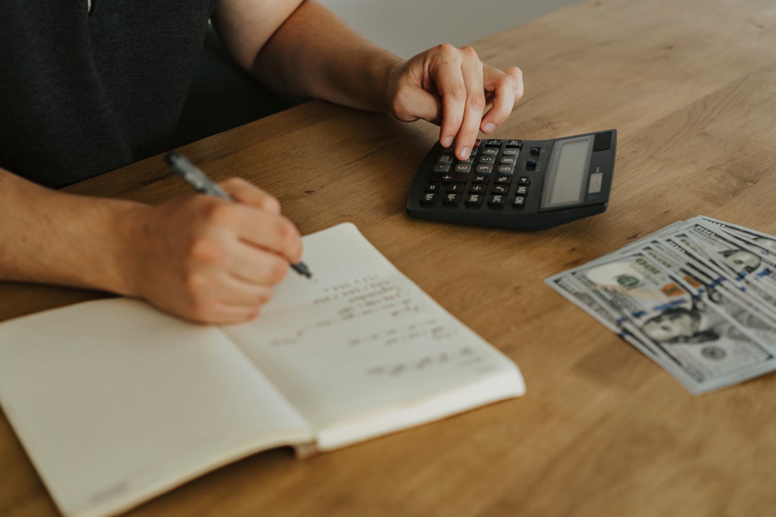 Mains sur une calculatrice, à côté d’un carnet et de billets