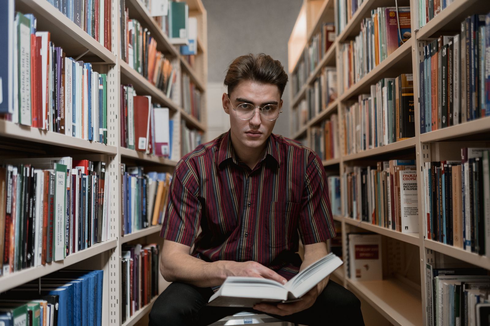 Étudiant lisant un livre entre les rayonnages d'une bibliothèque universitaire
